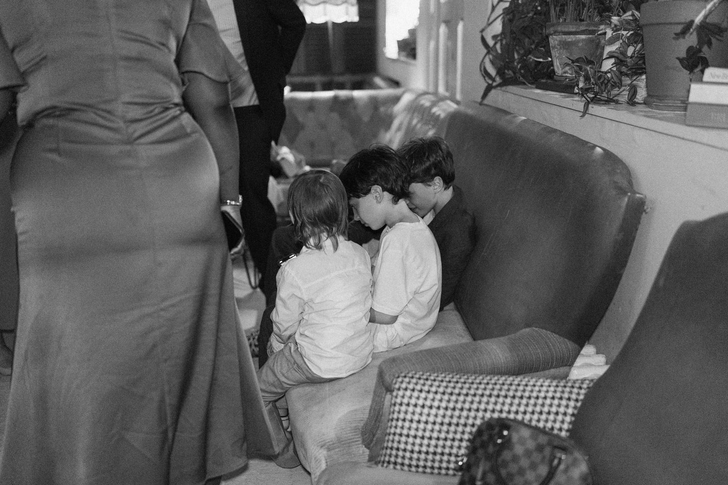 Black and white photo of two young children sitting together in an armchair at a wedding reception.