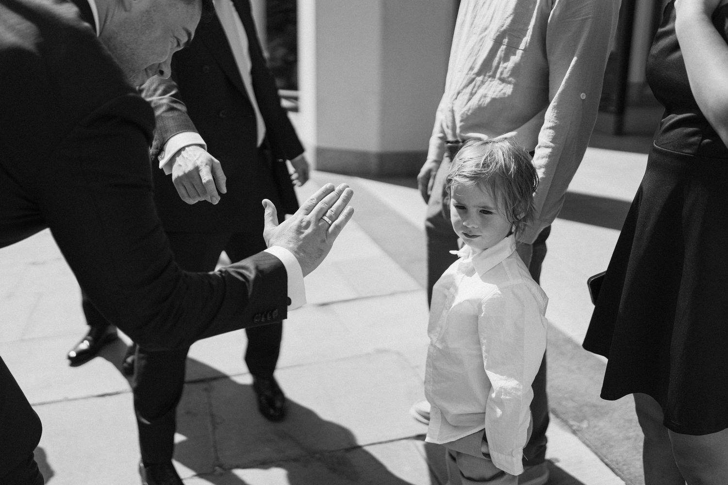 Black and white photo of young child giving a high five to adult guest at wedding ceremony.