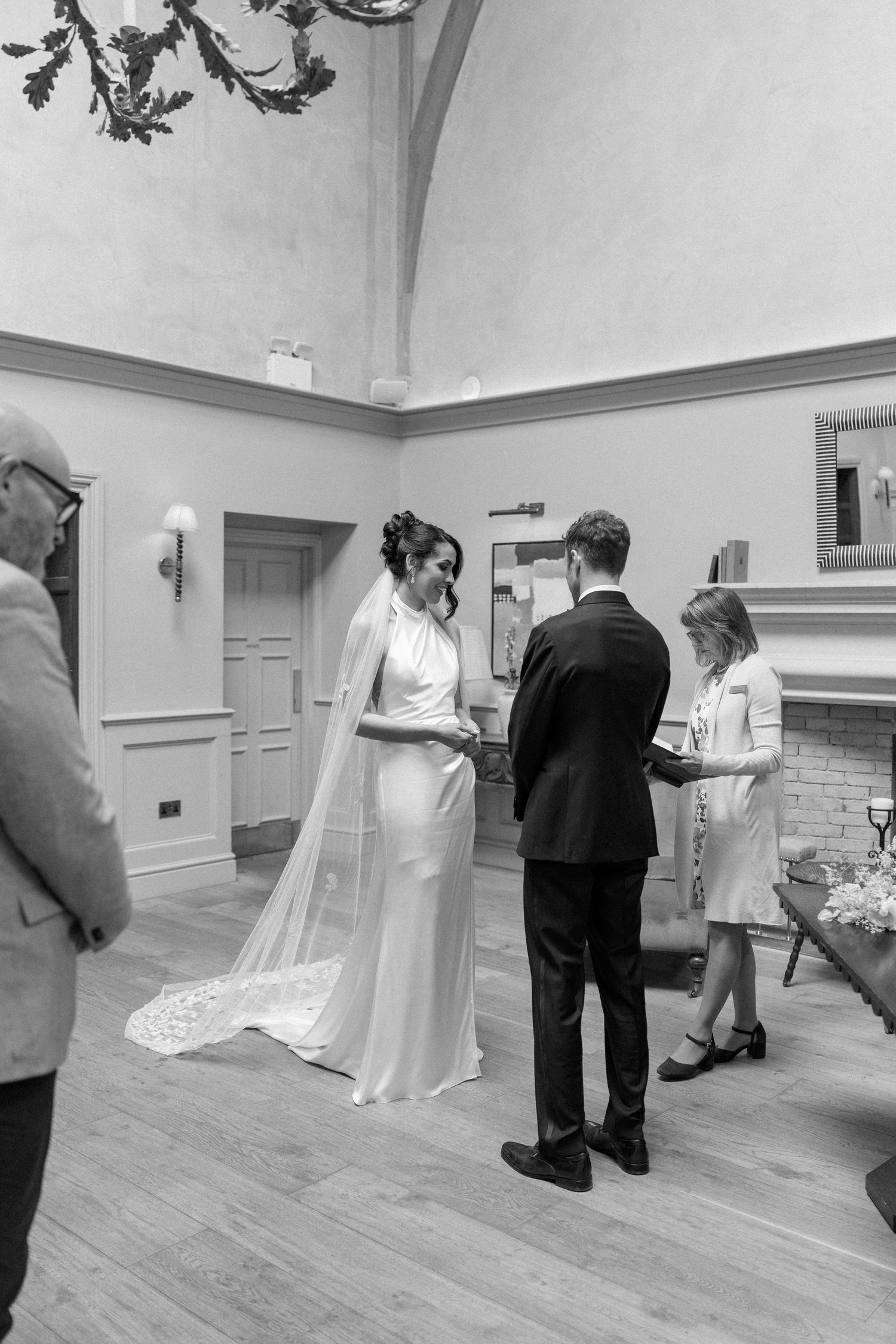 Black and white photo of bride and groom exchanging vows indoors during intimate wedding ceremony.