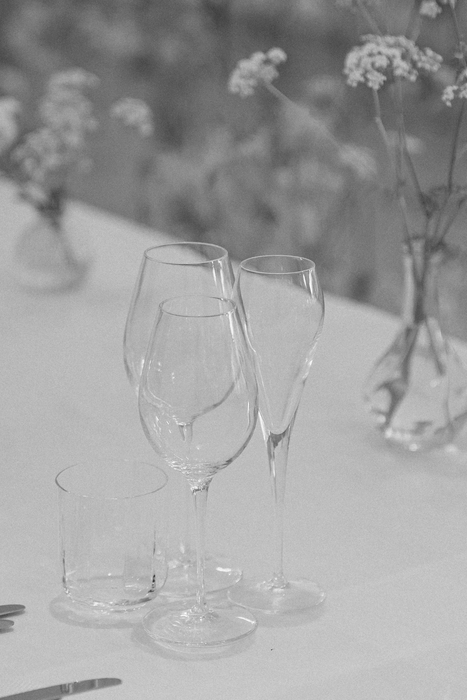 Black and white close-up of elegant wine and champagne glasses on white linen wedding reception table.