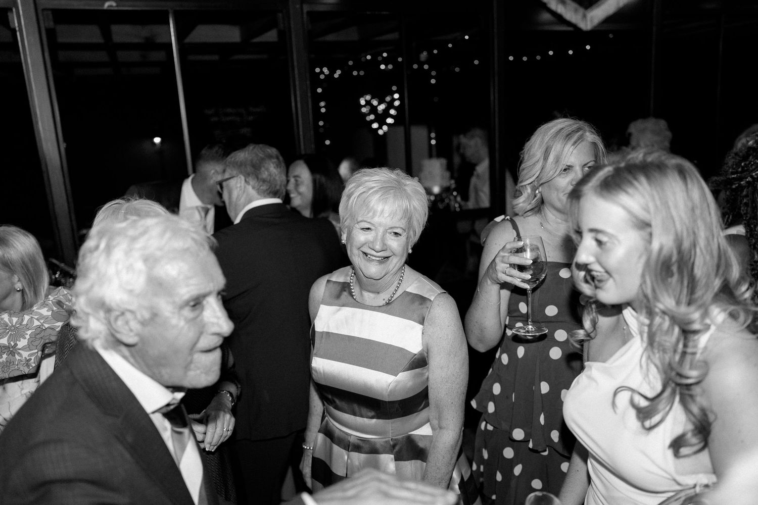 Black and white candid photo of wedding guests socializing and laughing at evening reception.