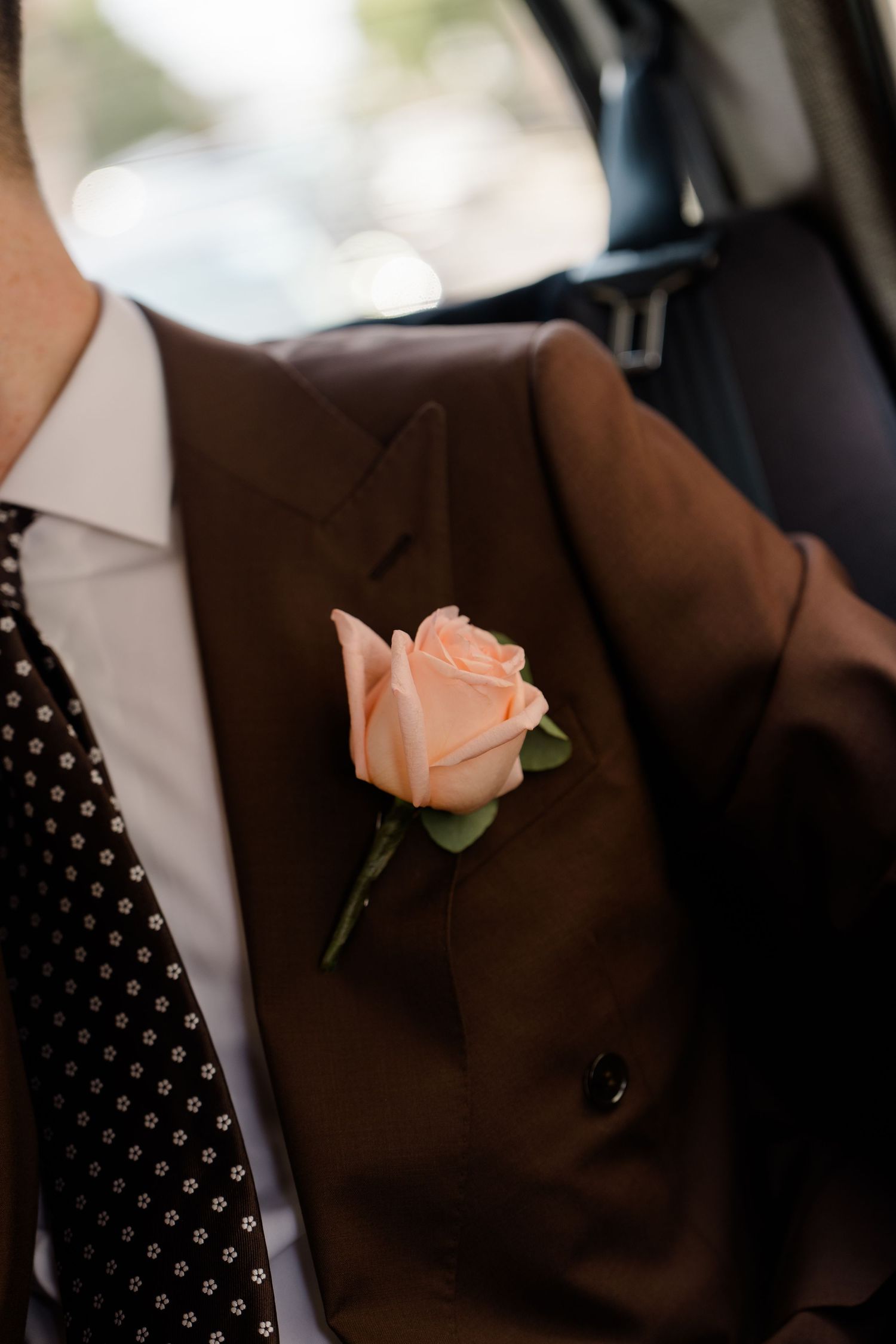 Close-up of peach rose boutonniere on grooms brown suit jacket with polka dot tie.