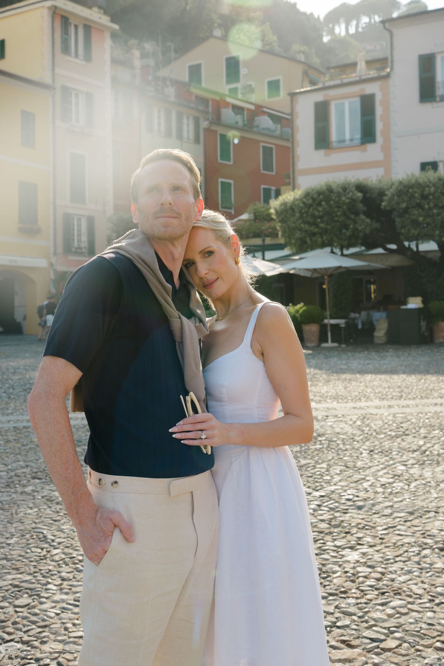 Elegant couple posing together in a sun-drenched cobblestone piazza in Portofino, Italy.