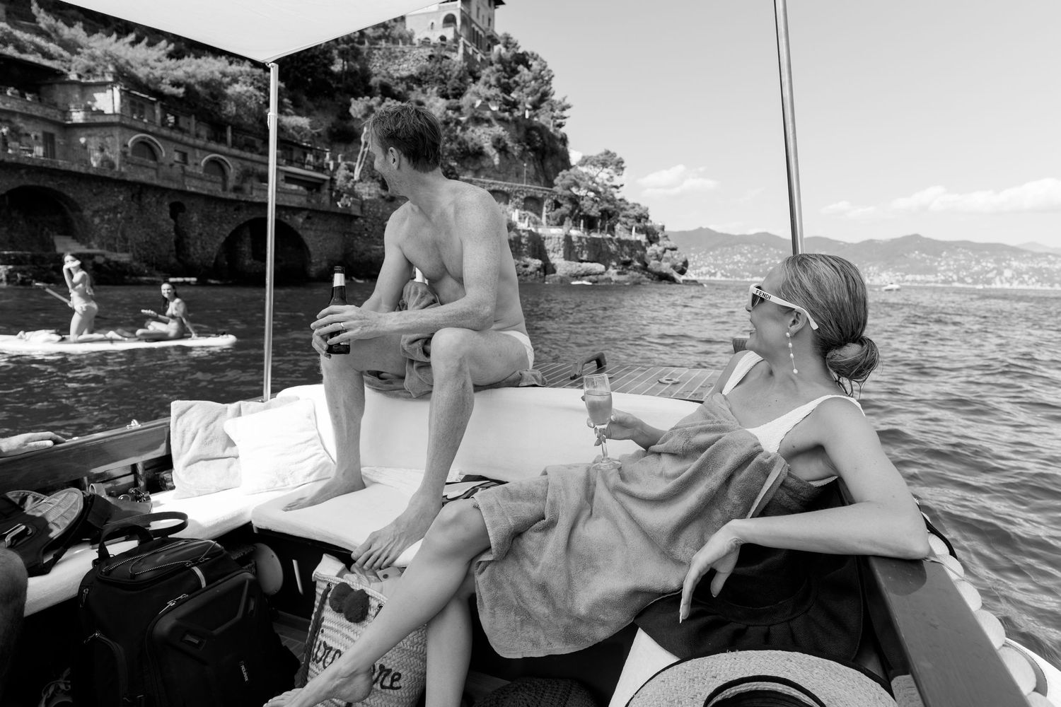 Black and white photo of a couple relaxing on a boat with a scenic coastal castle backdrop.