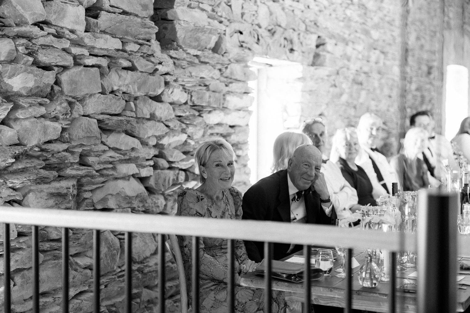 Black and white photo of an elegant wedding reception with stone walls and formal table settings.