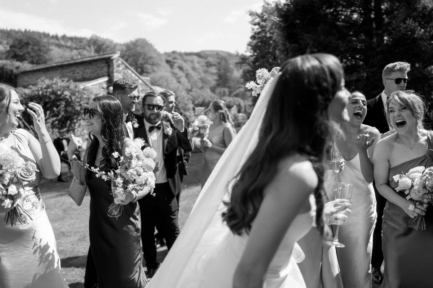 Black and white photo of wedding celebration with guests gathered outdoors on a sunny day.