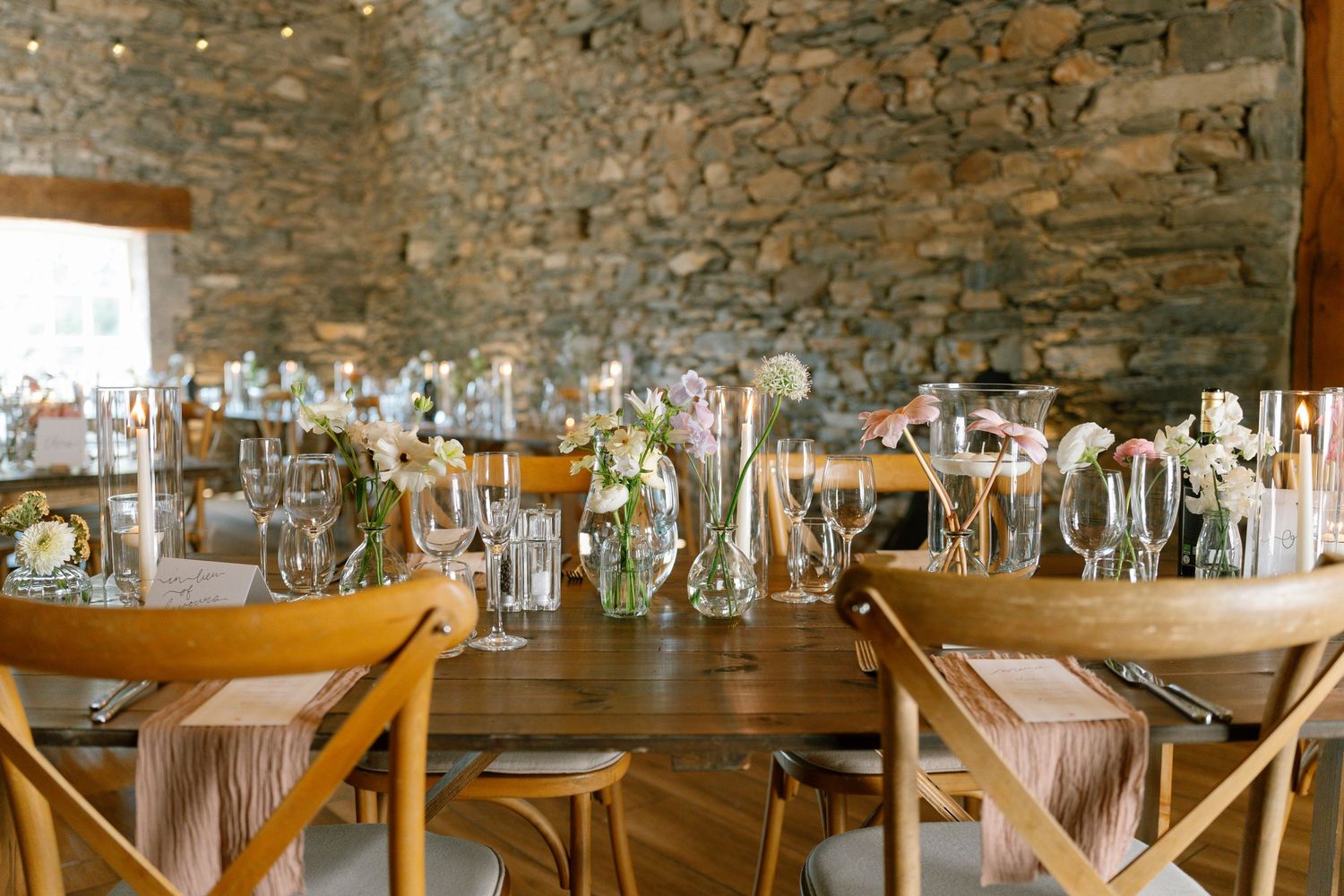 Stone-walled event space with wooden tables set up for a formal dining occasion.