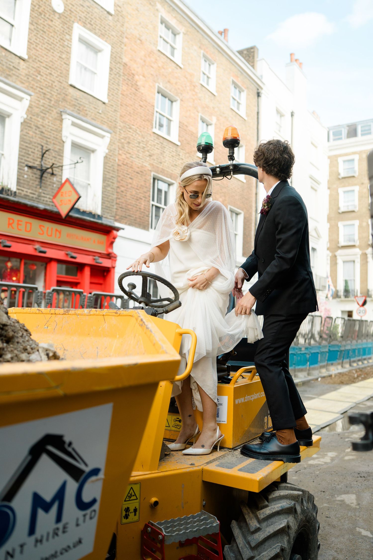 Playful wedding photos taken near a yellow construction vehicle on a city street.