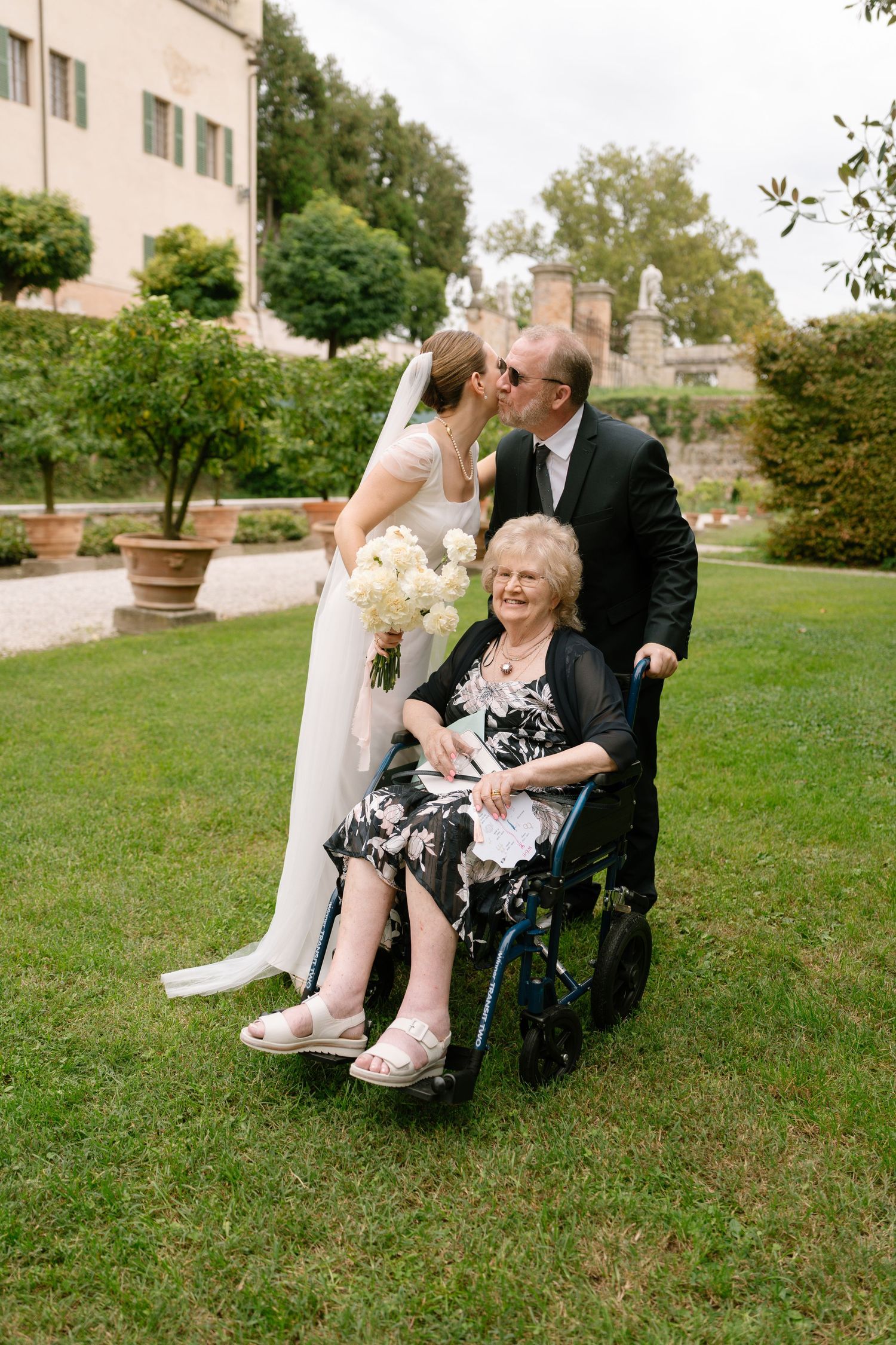 Wedding party members share joyful moments on a grassy lawn with historic architecture in the background.
