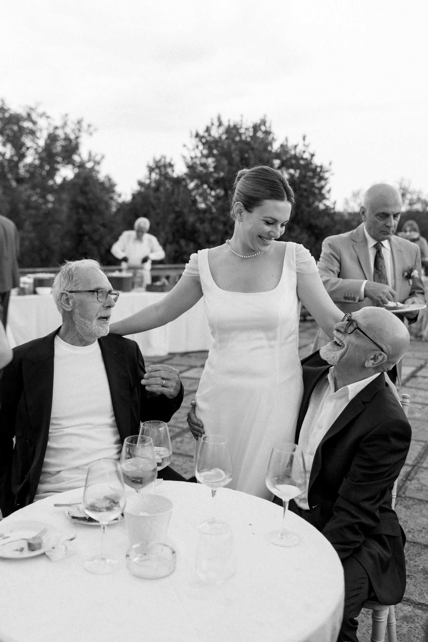 Black and white photo of wedding guests socializing at an outdoor reception table.