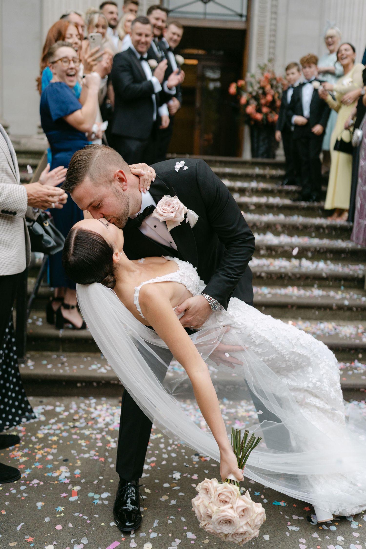 Dramatic wedding dip kiss on steps with confetti falling.