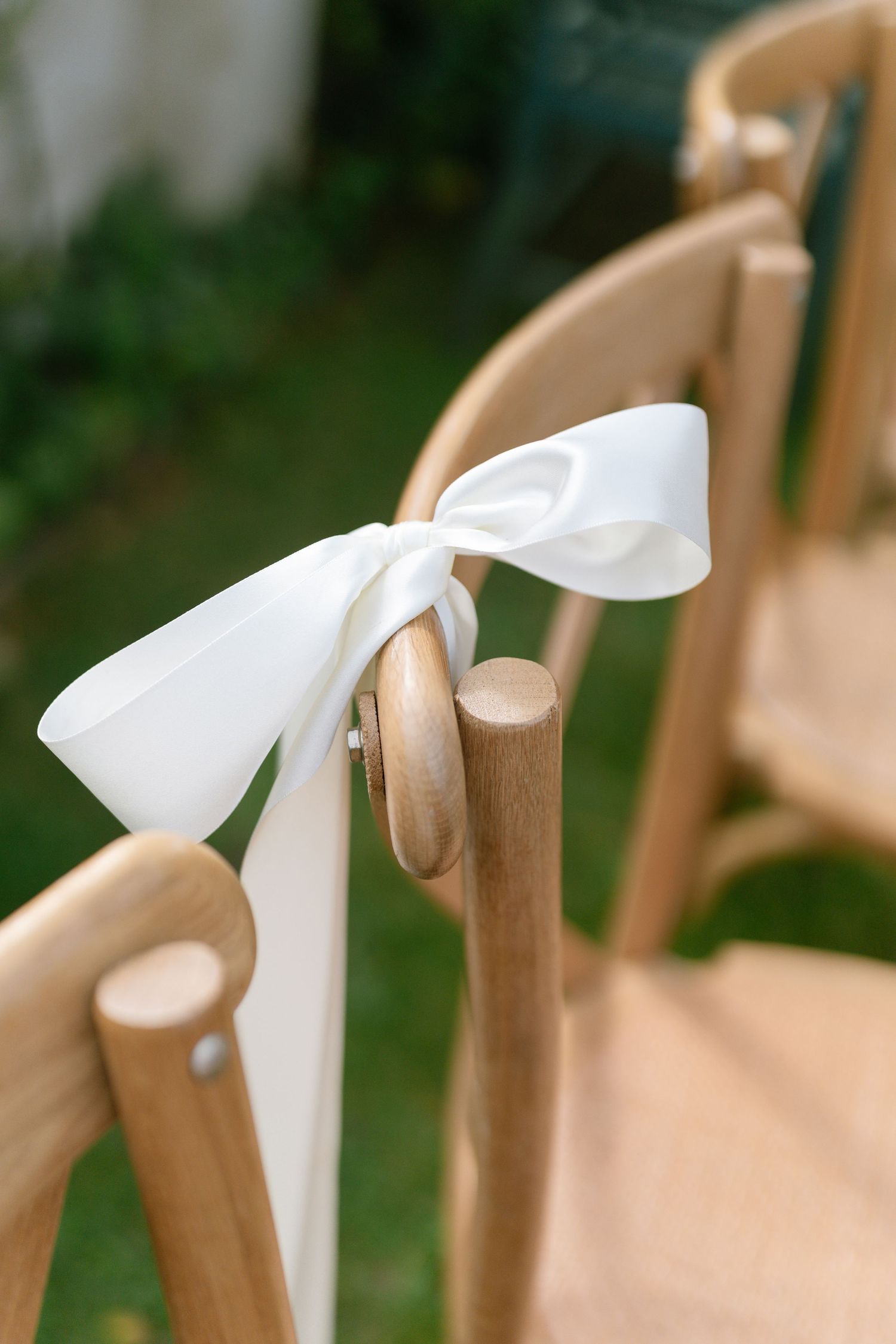 White ribbons tied elegantly around wooden chairs for an outdoor ceremony setup.