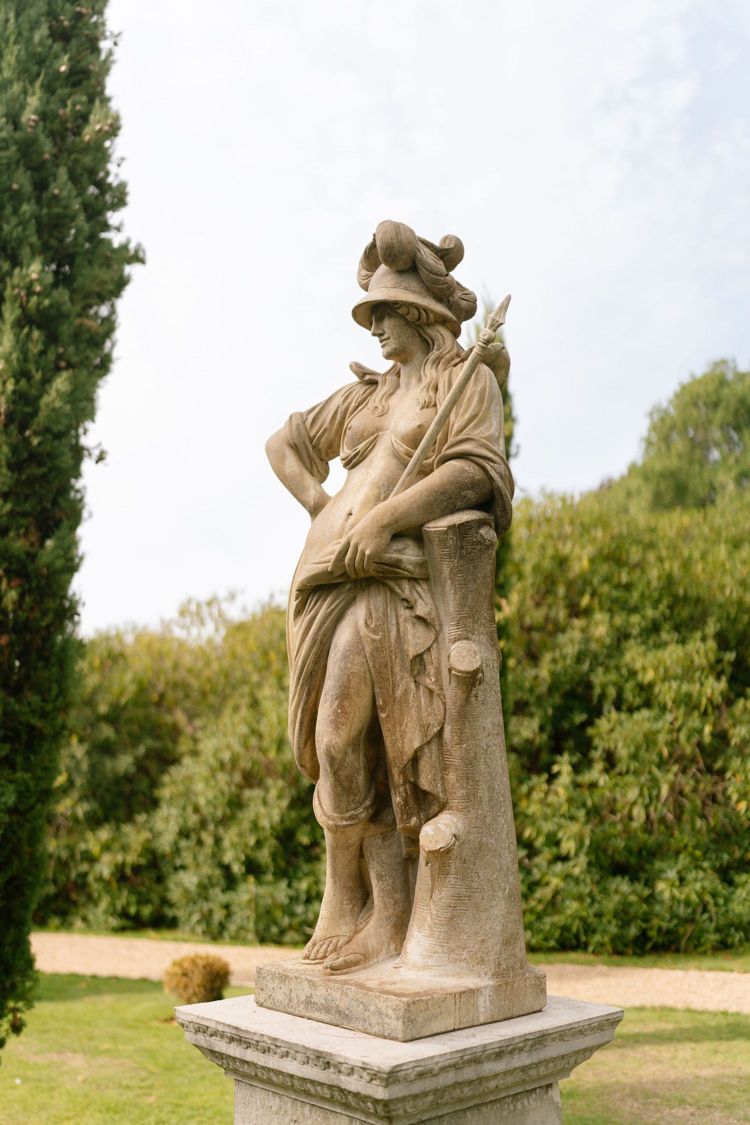 Stone sculpture of a seated figure with a hat in a garden setting.