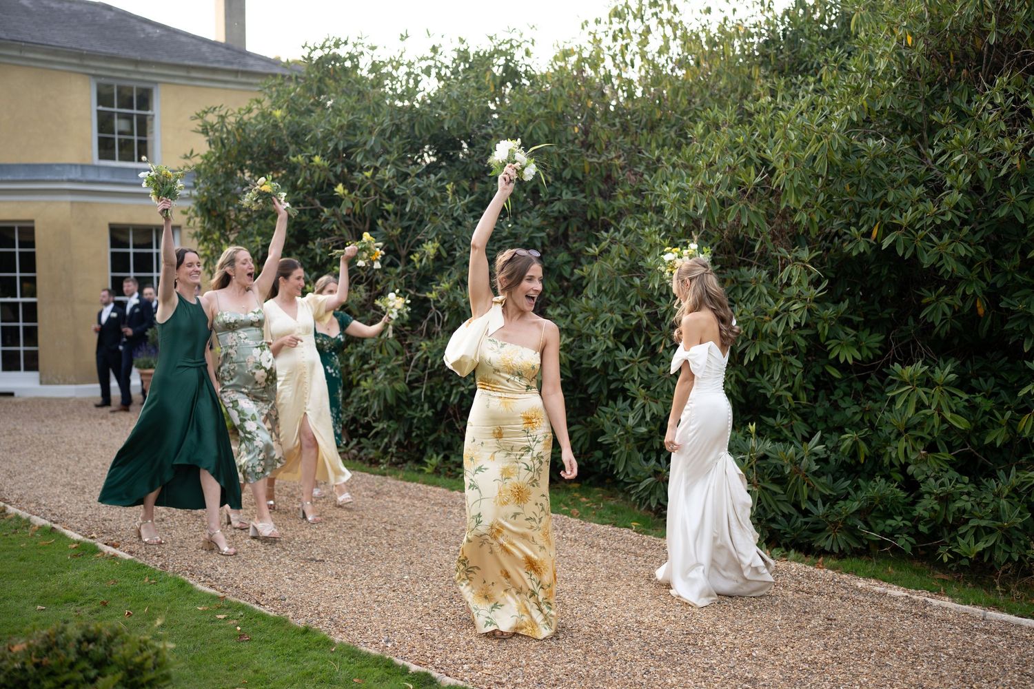 Wedding celebration group dances joyfully outside a yellow country house.