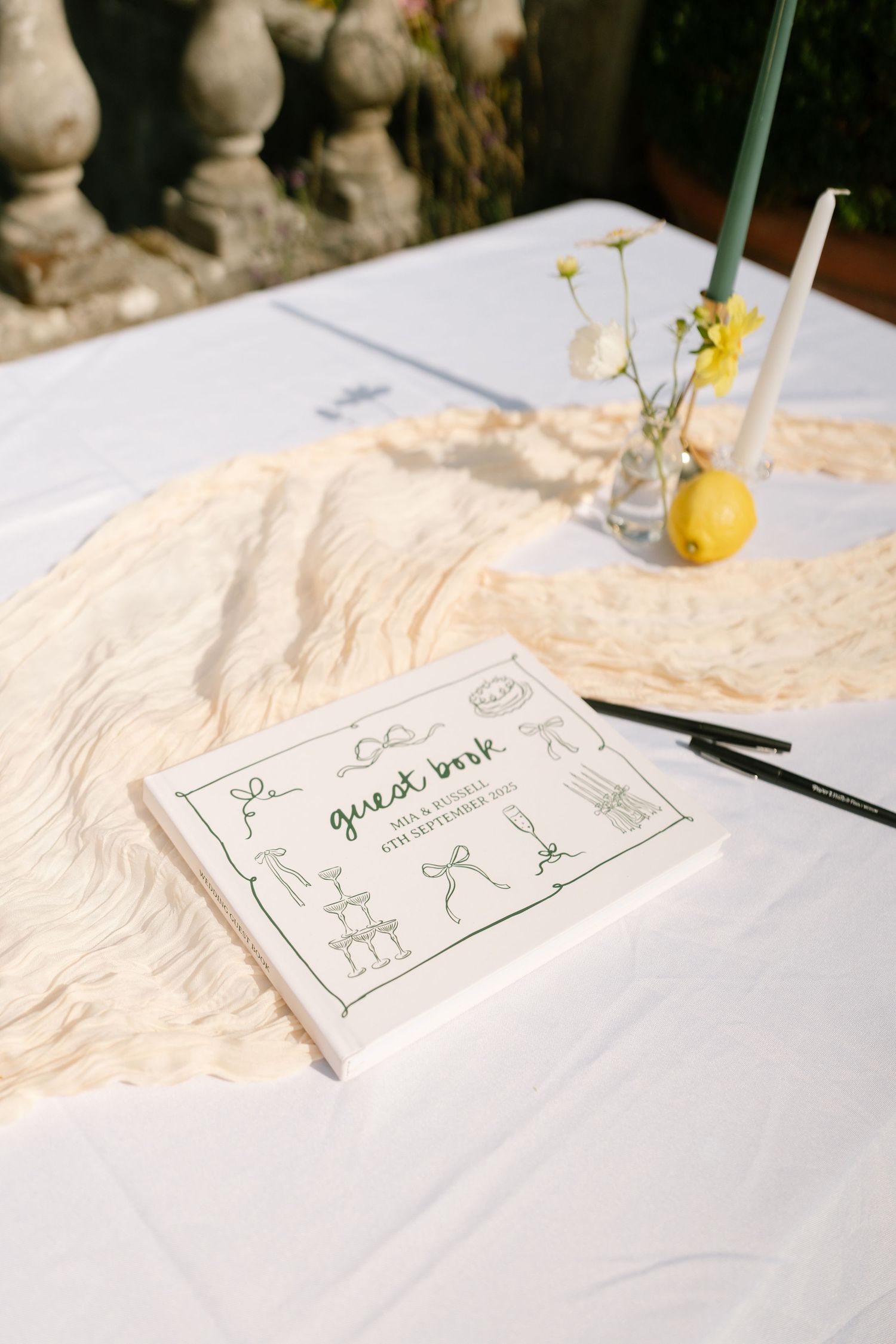 Simple wedding guest book with hand-drawn illustrations on a white tablecloth.