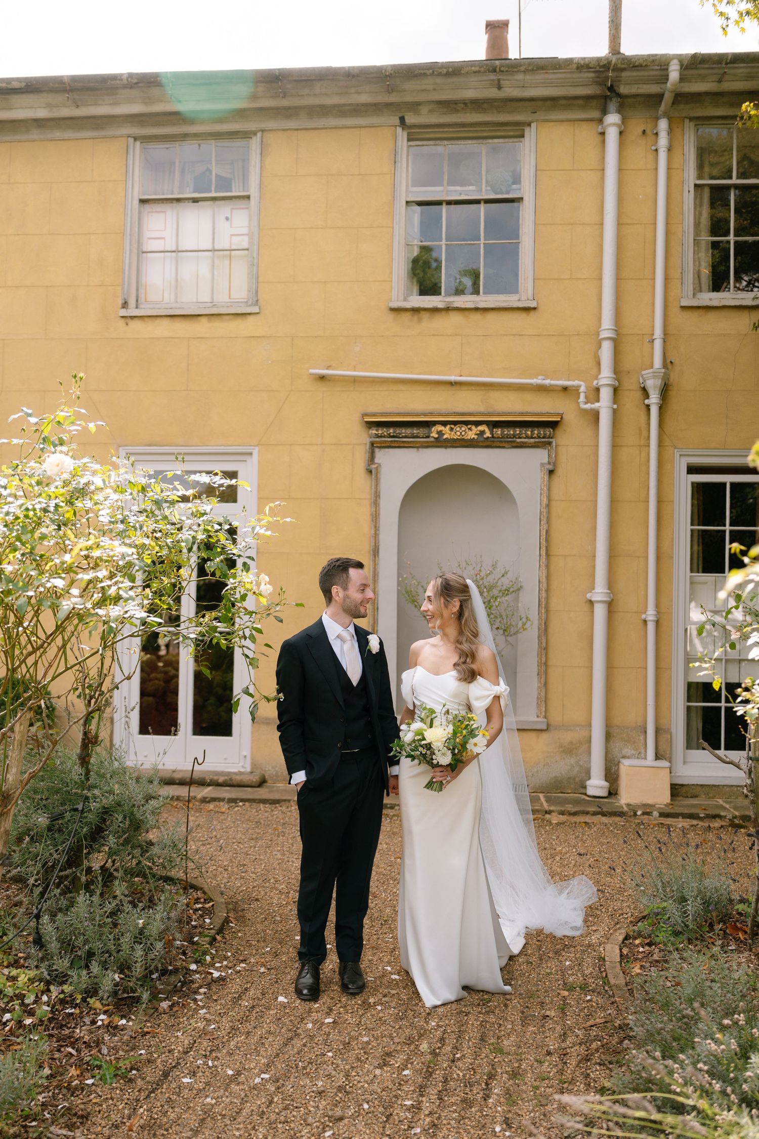 Romantic wedding scene outside yellow manor house with garden landscaping.