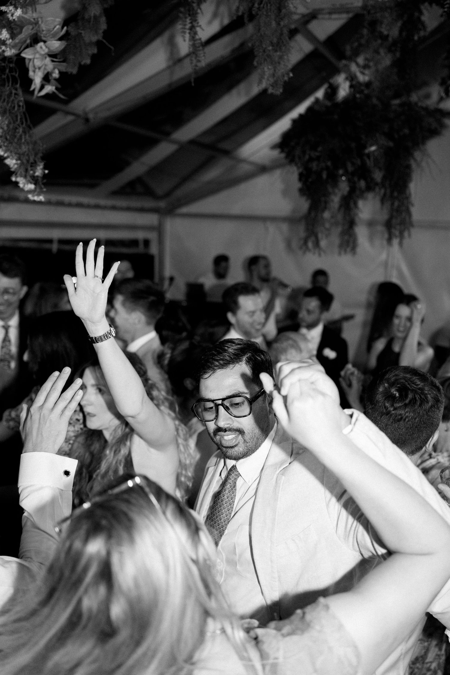 Black and white photo of party guests with raised hands dancing enthusiastically.