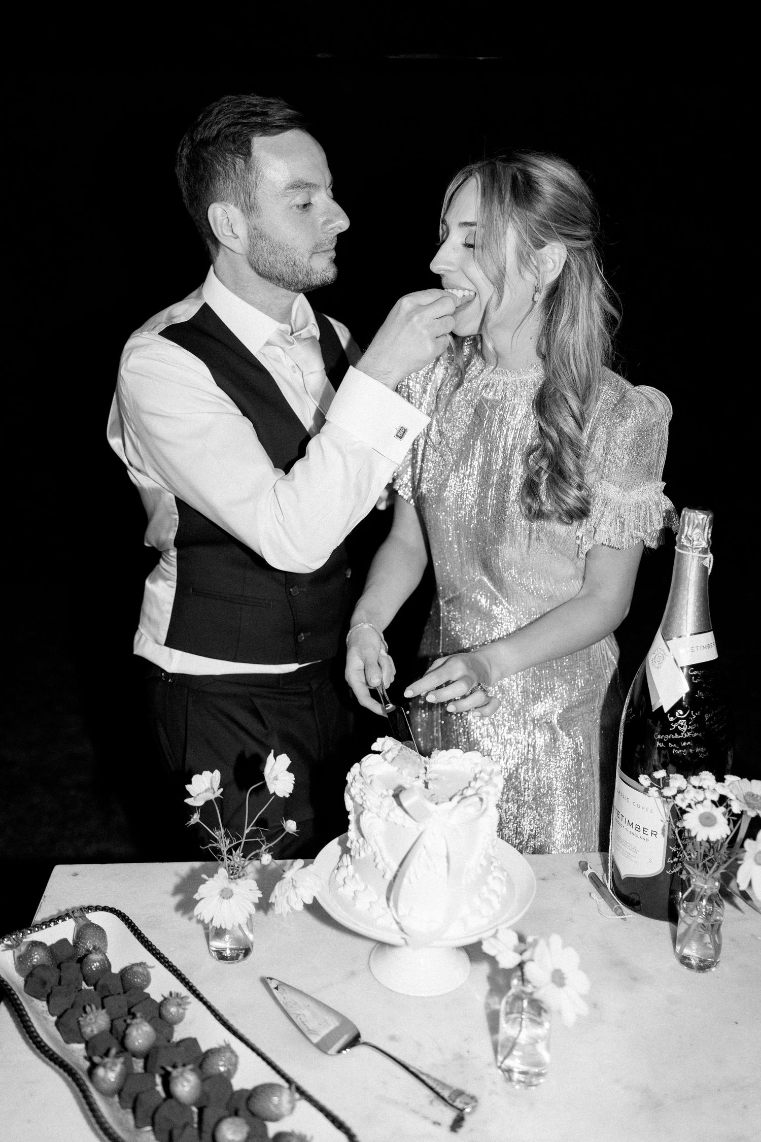 A couple shares a playful moment while cutting their wedding cake at an elegant reception.