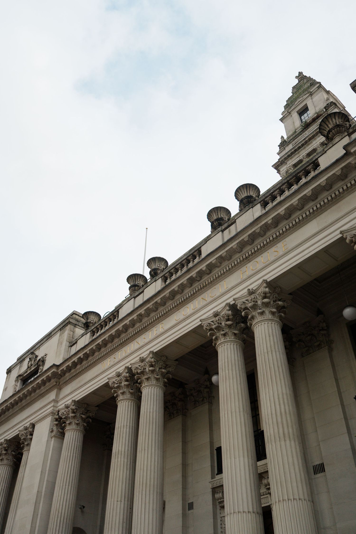 Grand neoclassical building with Corinthian columns and ornate tower against cloudy sky.