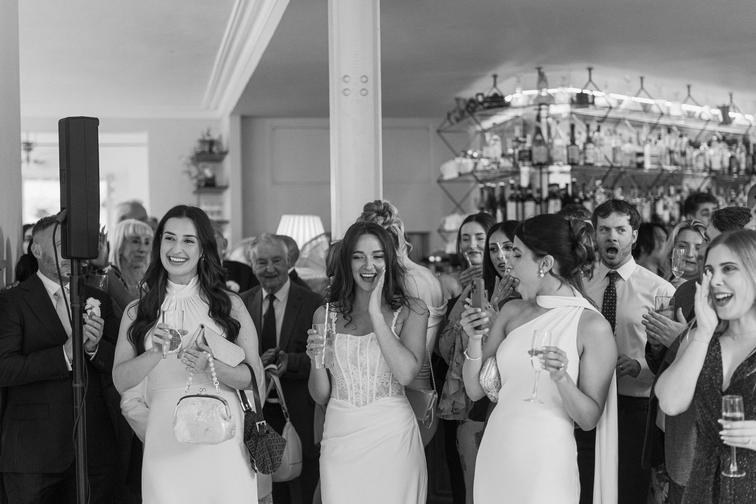 Wedding guests in white dresses laughing and celebrating together at elegant indoor reception venue.