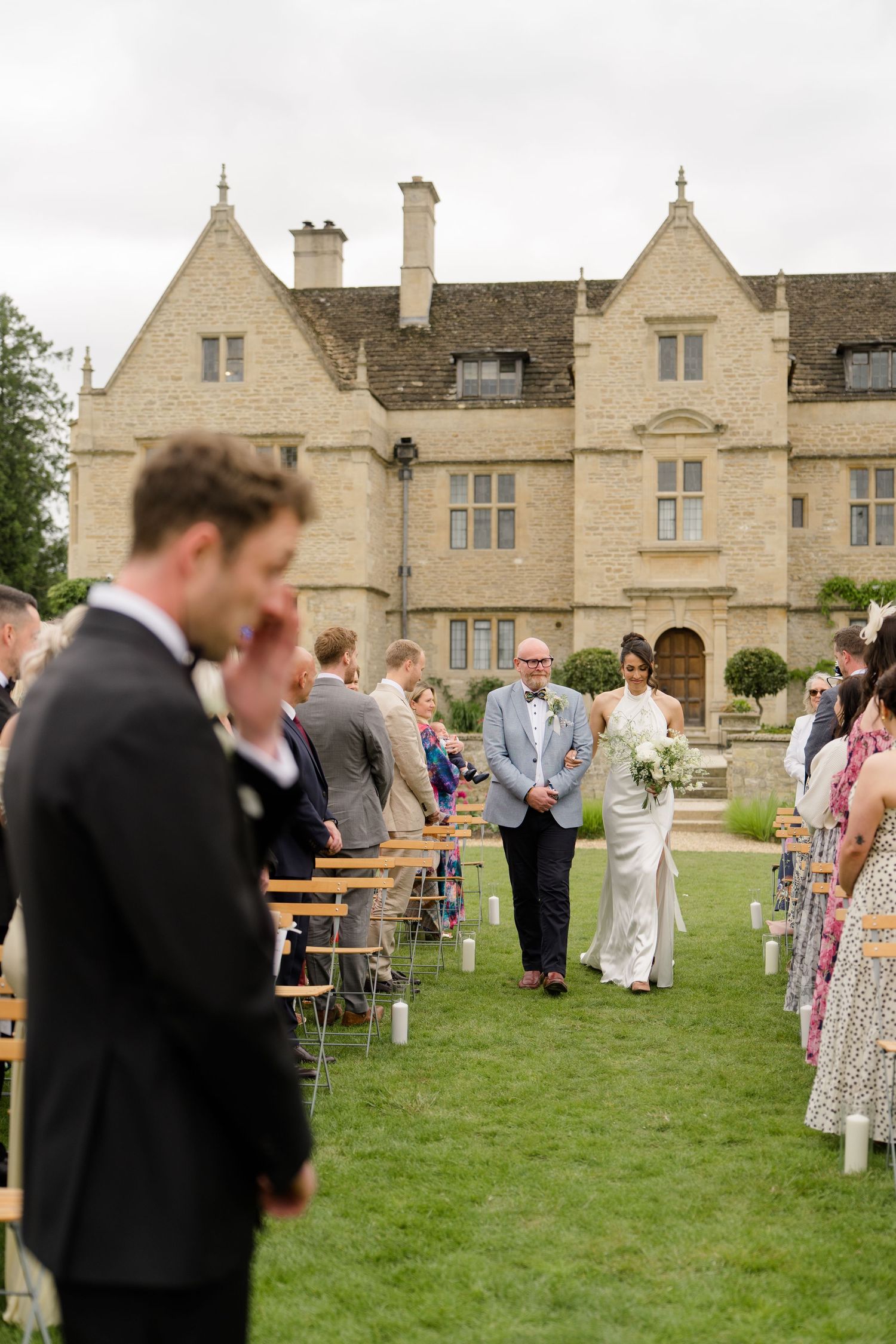 Bride walking down the aisle with her father toward the groom at an outdoor manor house wedding.