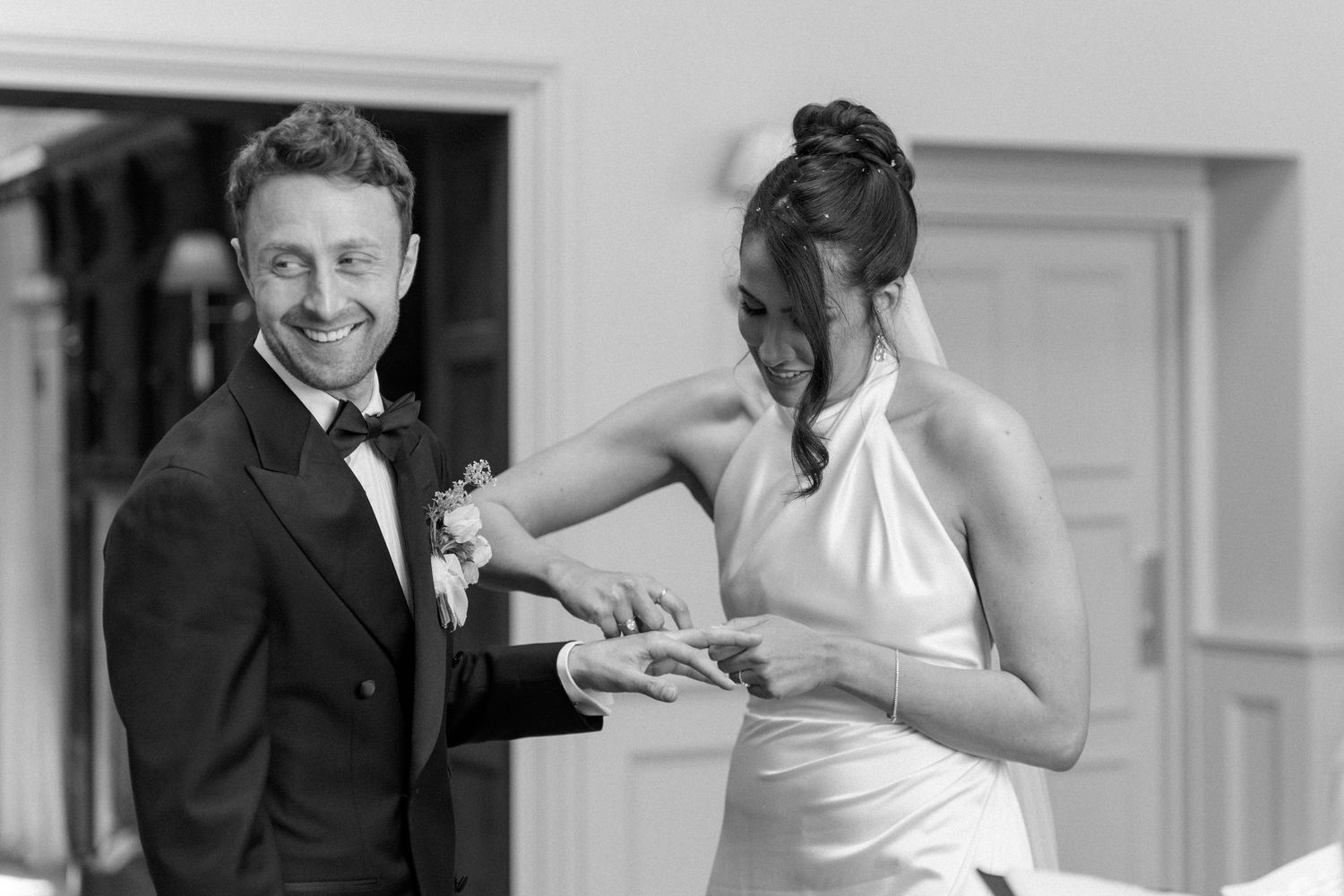 Groom smiles as bride reads vows during black and white outdoor wedding ceremony.