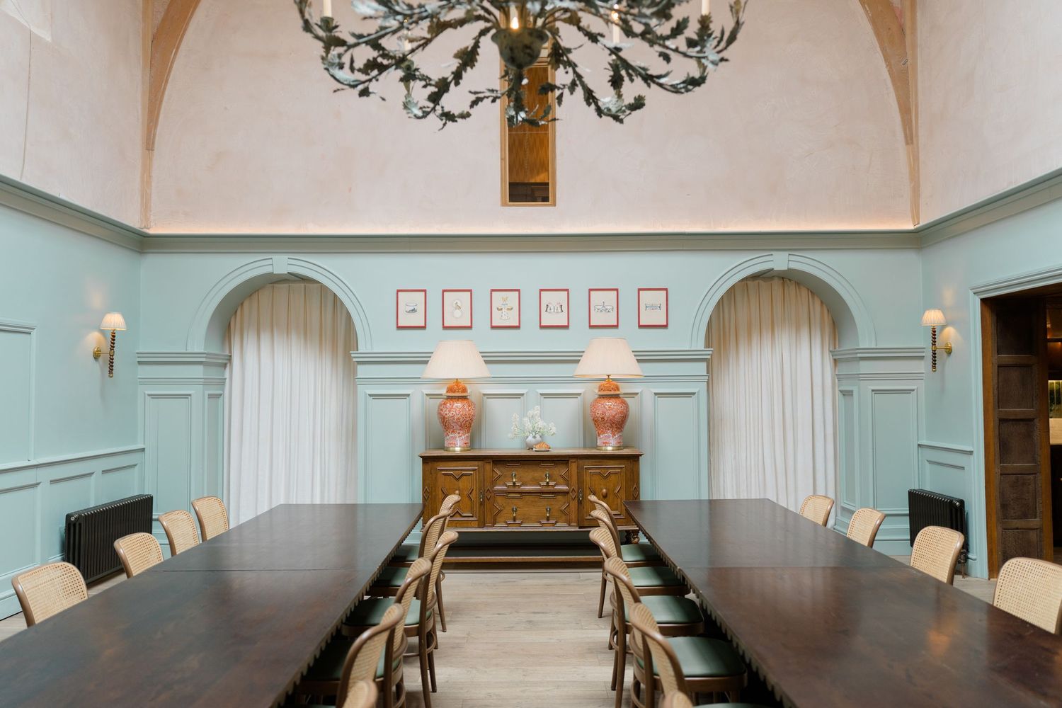 Elegant dining room with mint green walls, arched alcoves, dark wood table, cream chairs, ornate chandelier, and pink framed artwork.