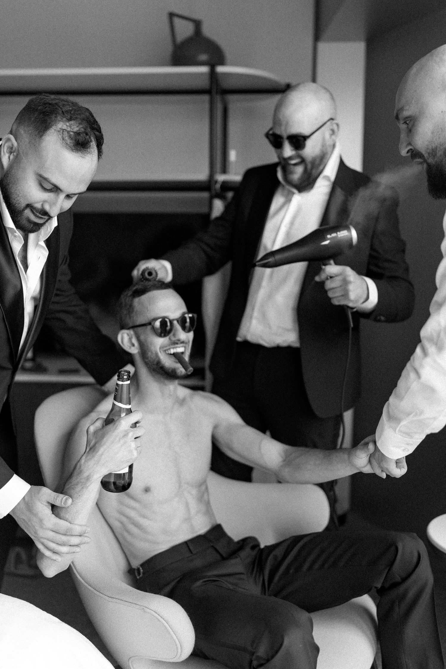 Groomsmen in black suits and sunglasses laughing together during wedding preparations.