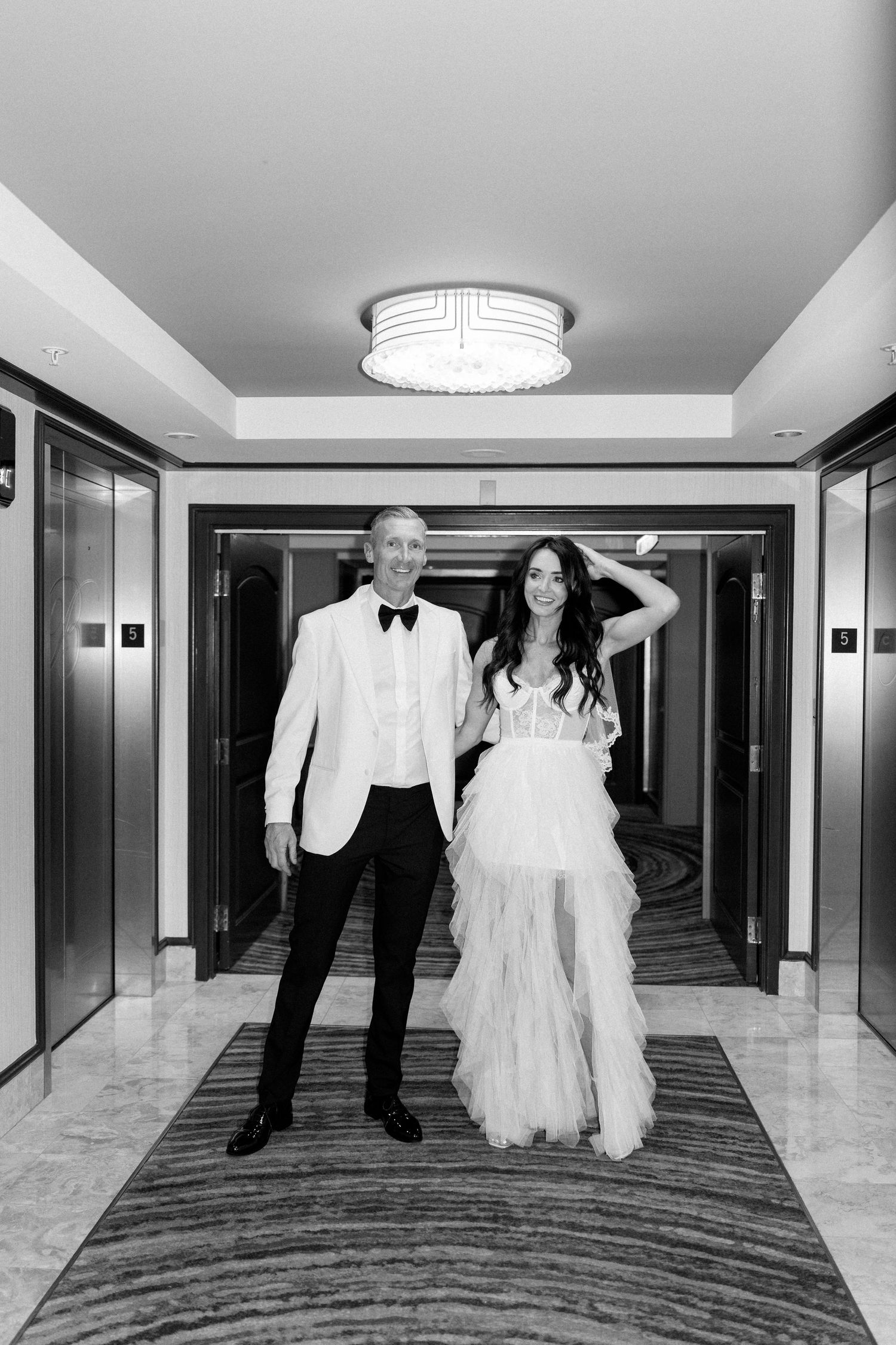 Wedding couple walks playfully down a modern hotel hallway with marble floors.