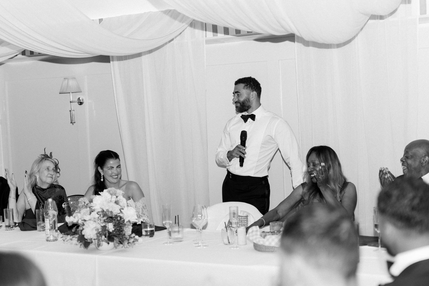 Black and white photo of best man delivering speech at elegant wedding reception dinner.