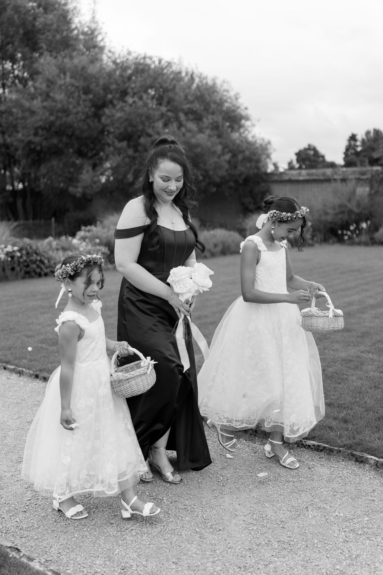 Black and white photo of a bridesmaid walking with two flower girls carrying baskets.