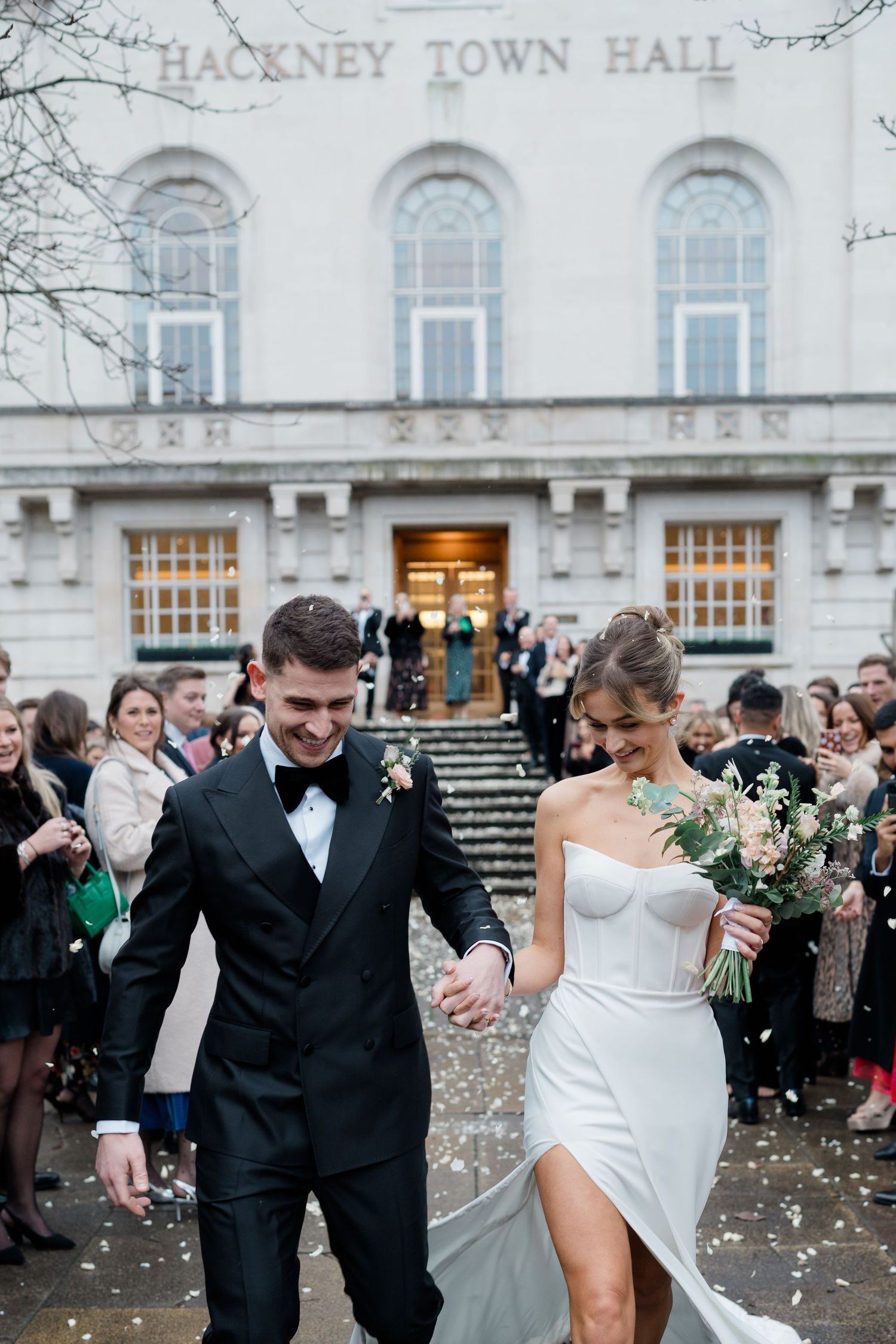 A couple exits Hackney Town Hall during their wedding celebration as guests throw confetti on the historic building's steps.