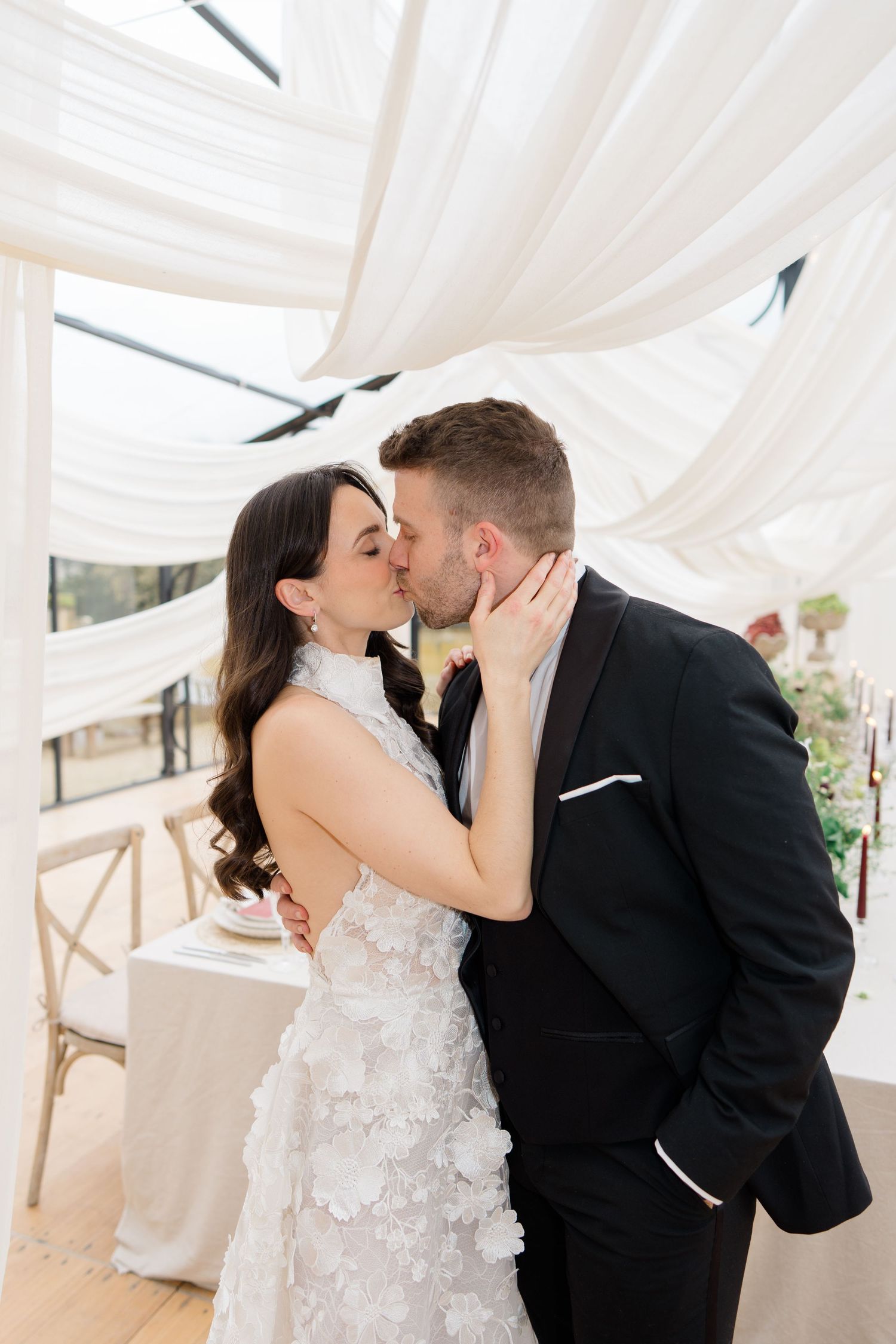 Intimate wedding moment captured under white draped tent with soft lighting.