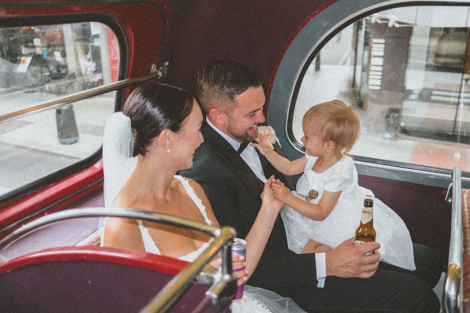 A couple and young child share a sweet moment together in the back seat of a vintage red car.