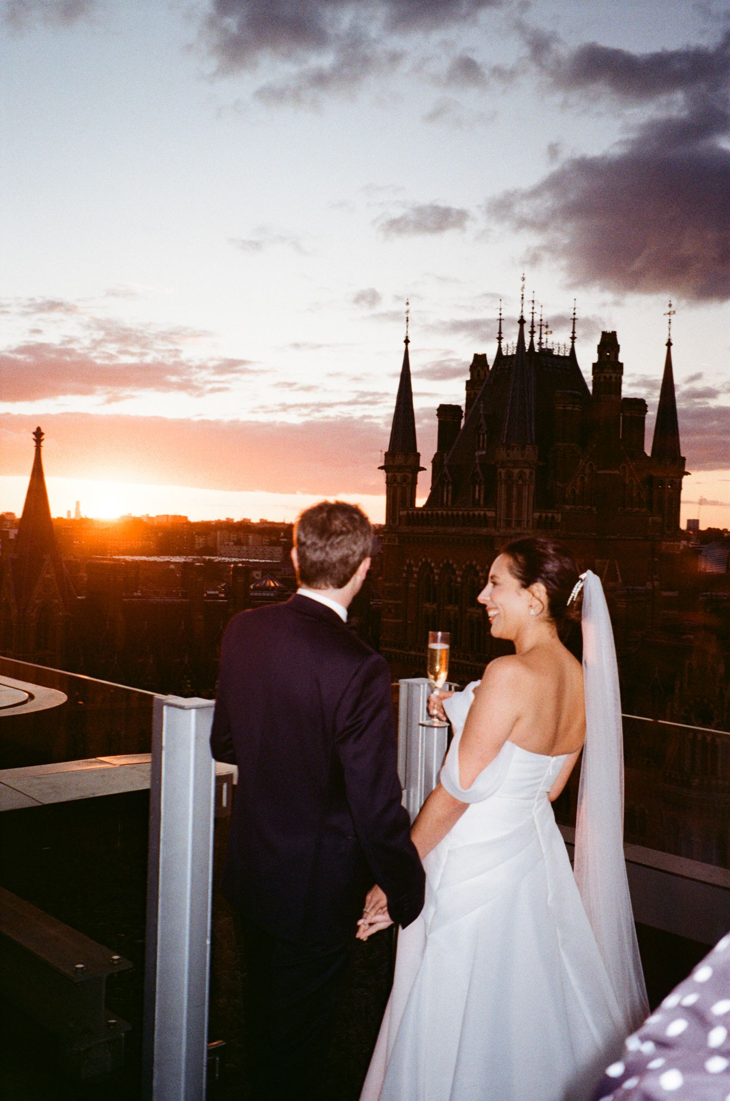 A couple enjoys sunset views of historic architecture silhouettes from a rooftop vantage point.
