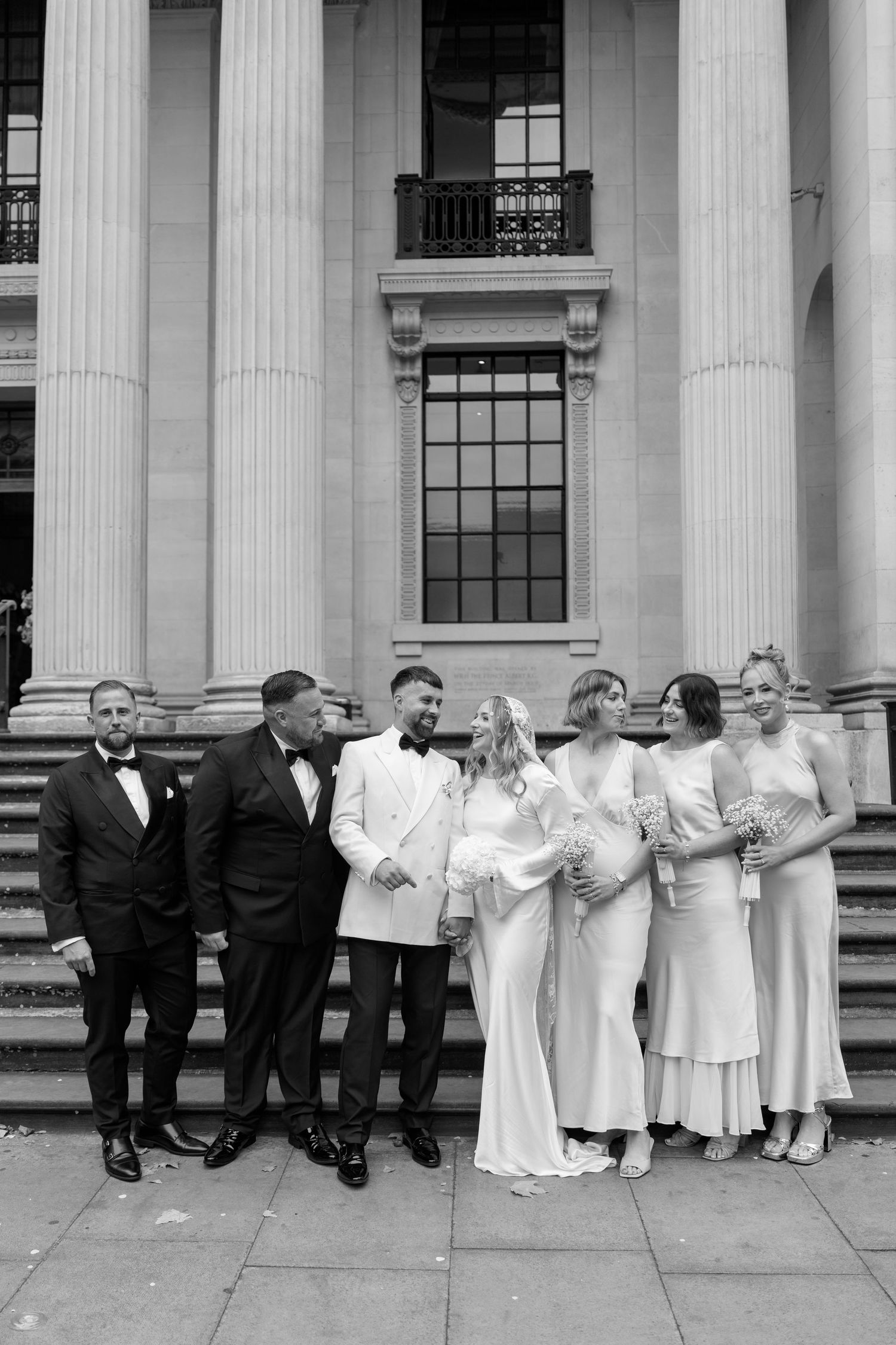 Wedding party poses along classical columns in black and white formal attire.