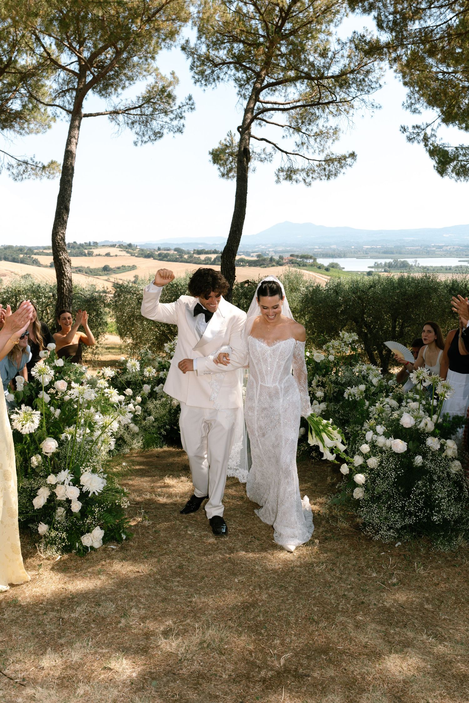 Outdoor wedding processional along a flower-lined path with mountain views.