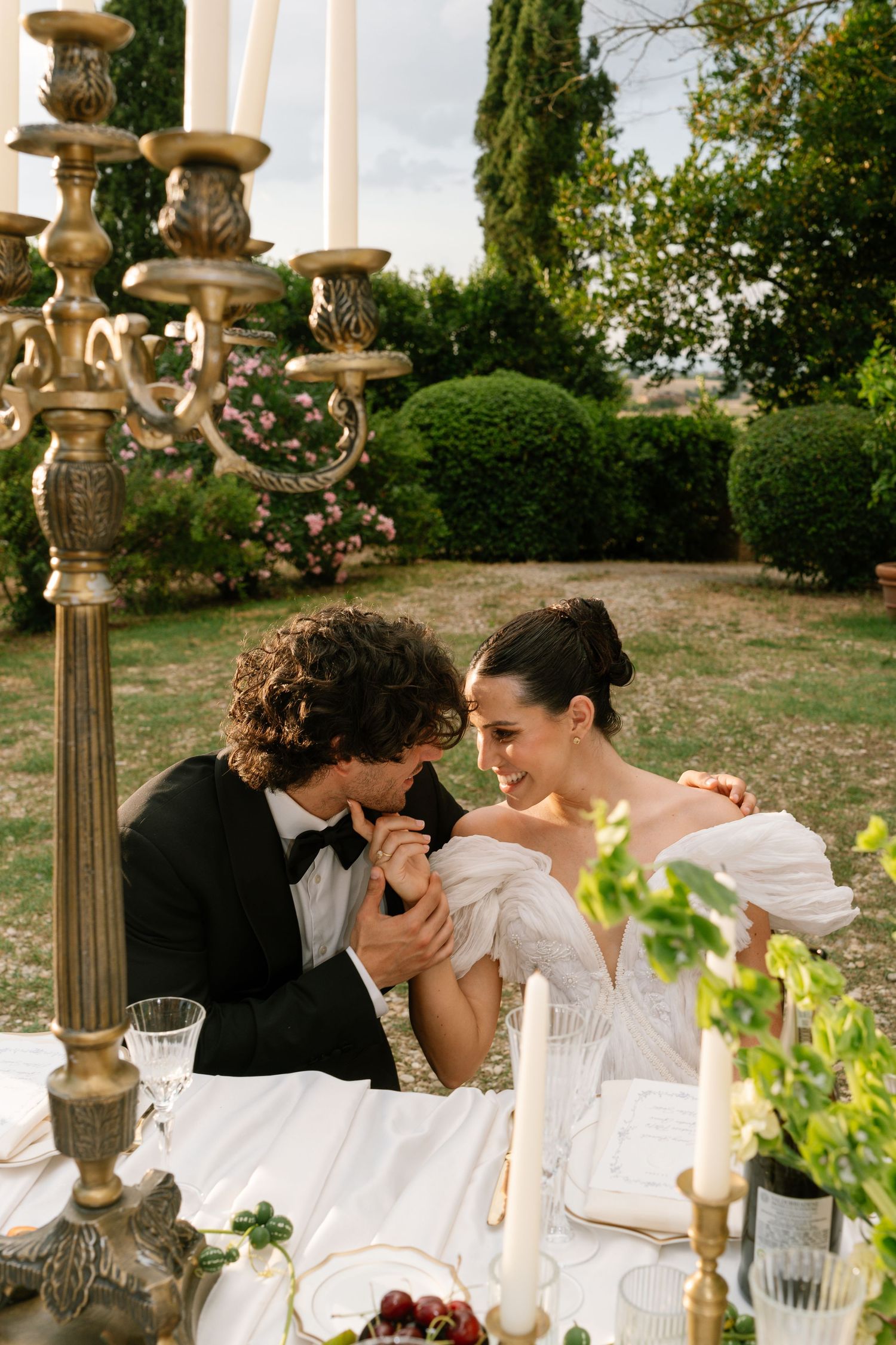 Outdoor wedding reception table with elegant candelabras and white table settings under natural lighting.