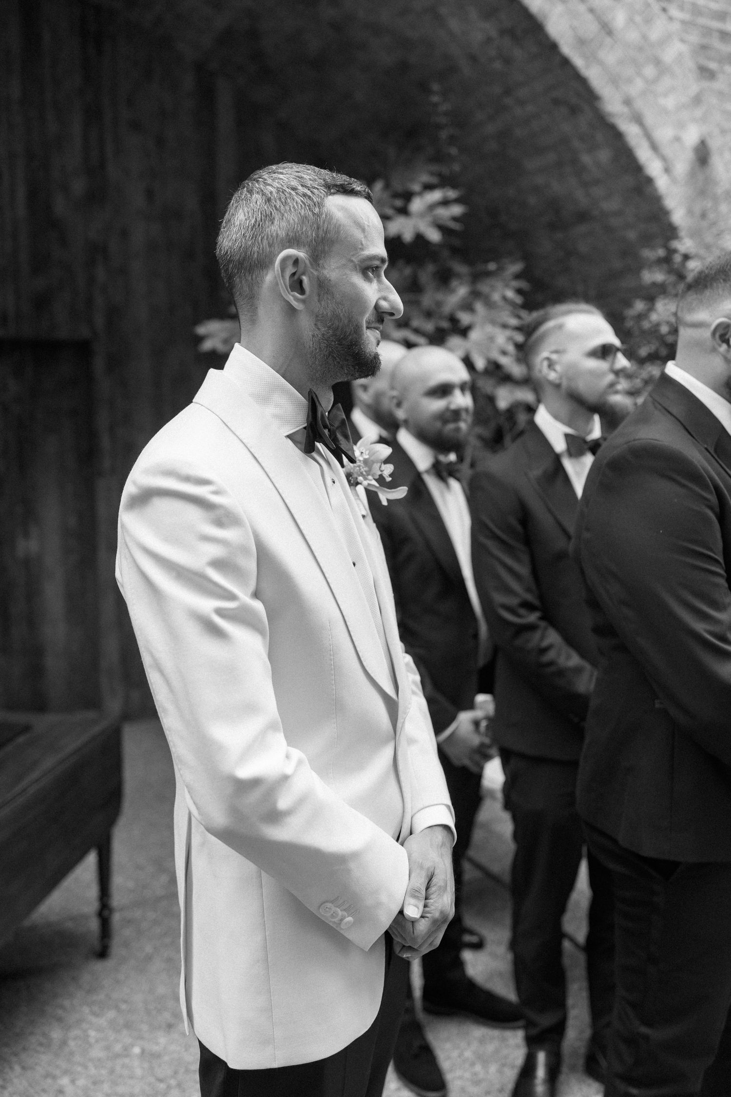 Groomsmen in formal attire sharing laughs and conversations outdoors.