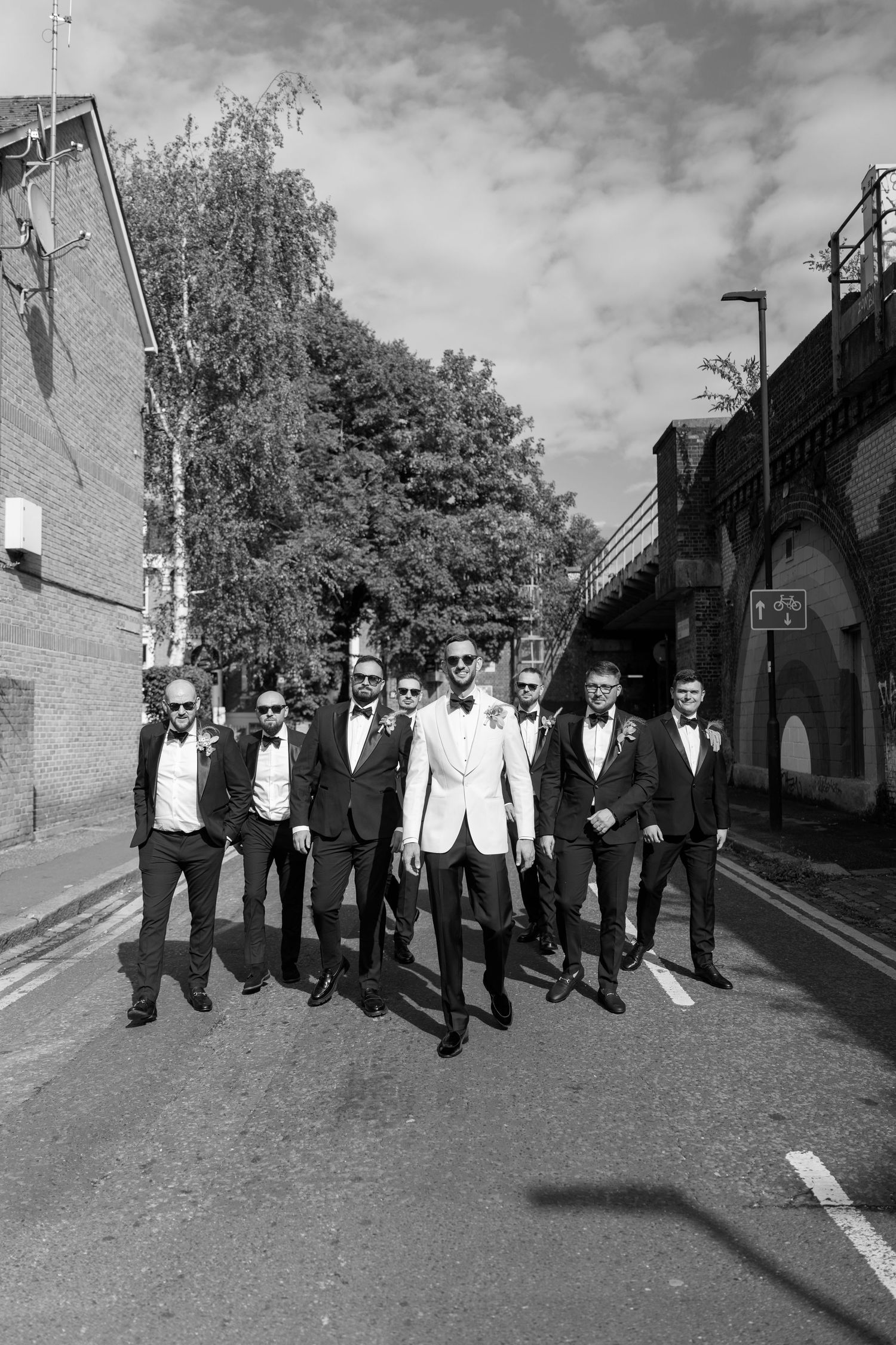 Groomsmen in formal black and white attire walking together down a street.