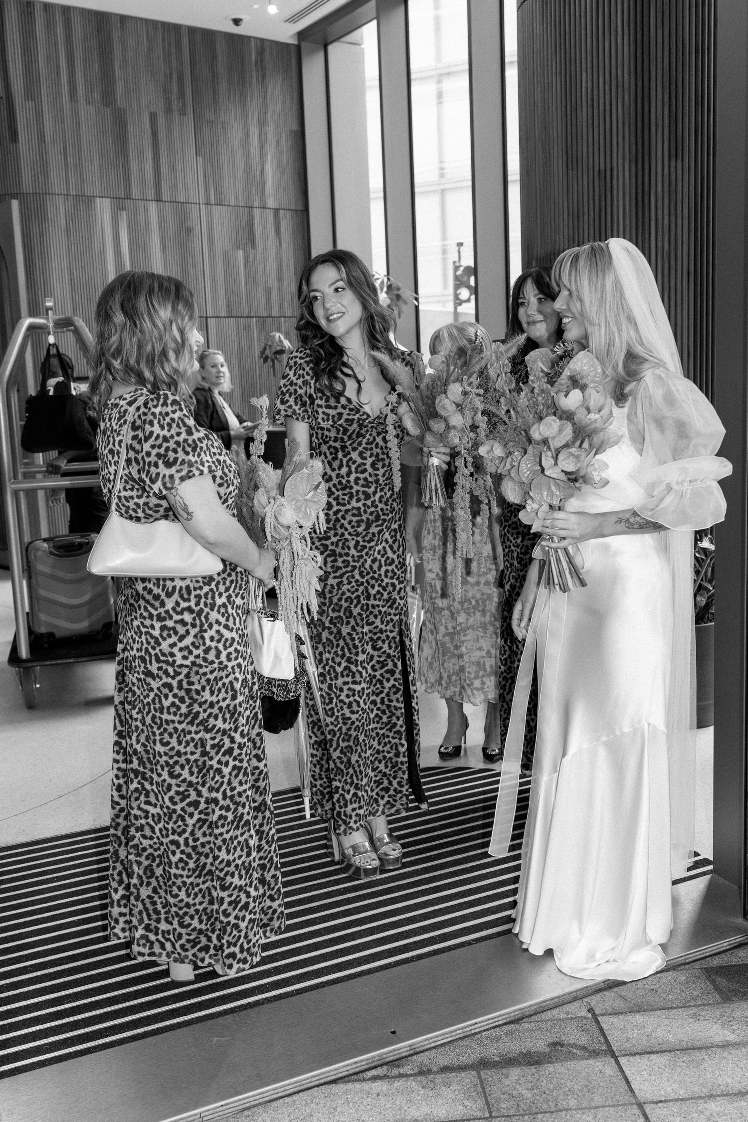 Wedding party in leopard print dresses and white gown posing together in front of mirrors.