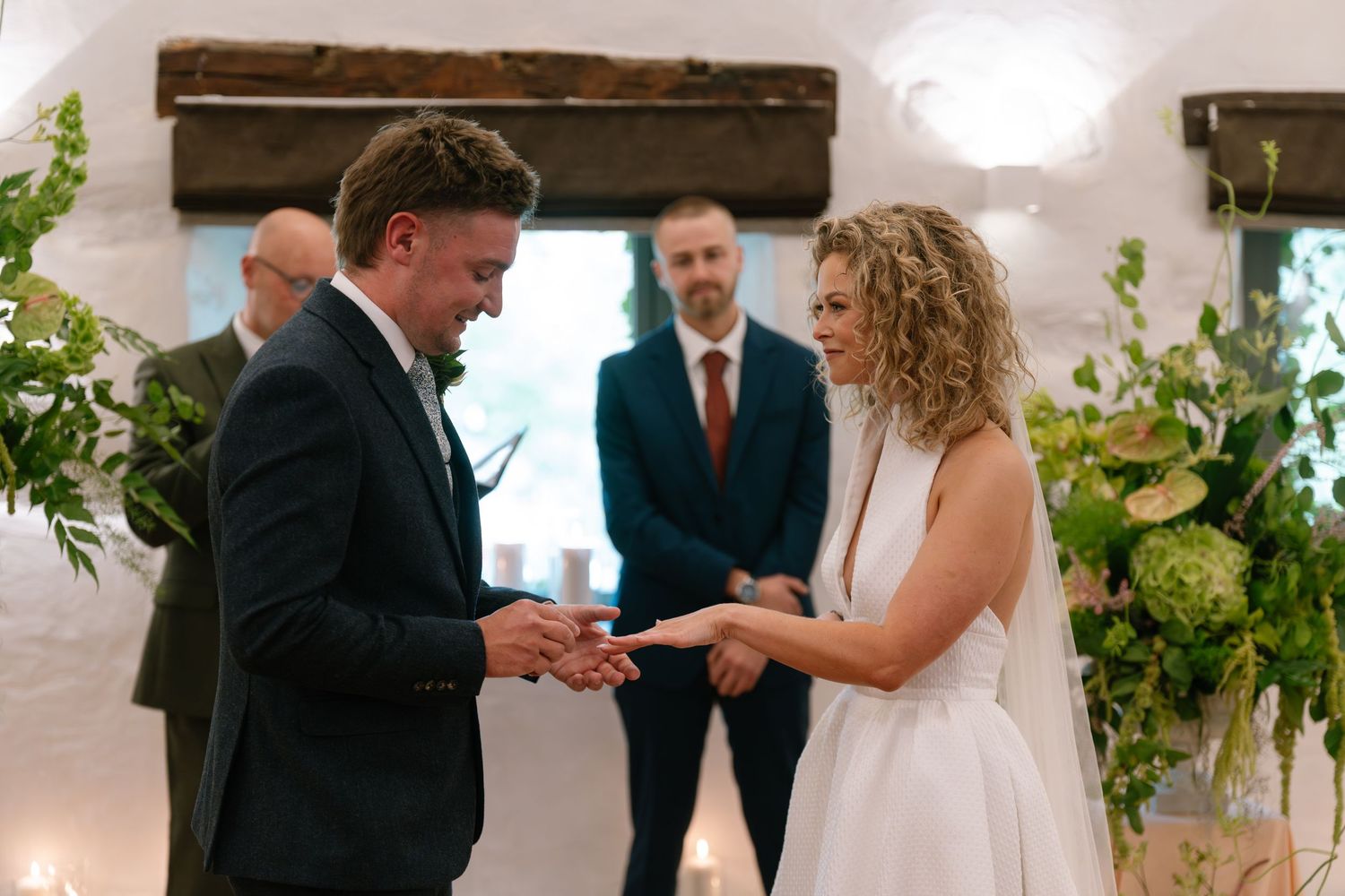 A wedding ceremony in progress with guests gathered in a bright indoor venue decorated with greenery.