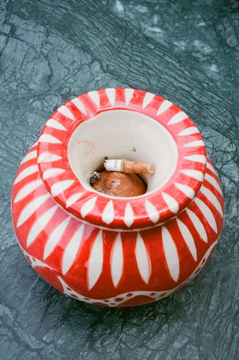 Red and white ceramic Moroccan ashtray with cigarette butts on marble surface.