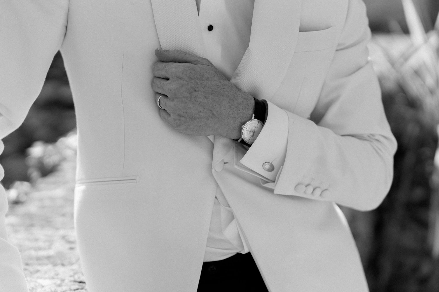 Close-up black and white detail of groom in white tuxedo jacket with luxury watch and cufflinks.