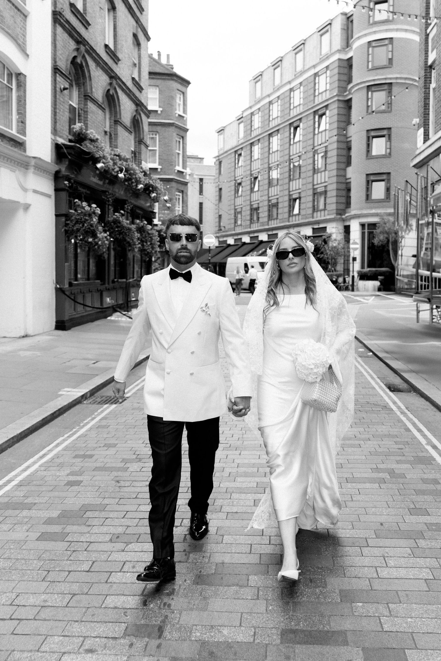 Newlyweds strolling down a cobblestone street in formal wedding attire.