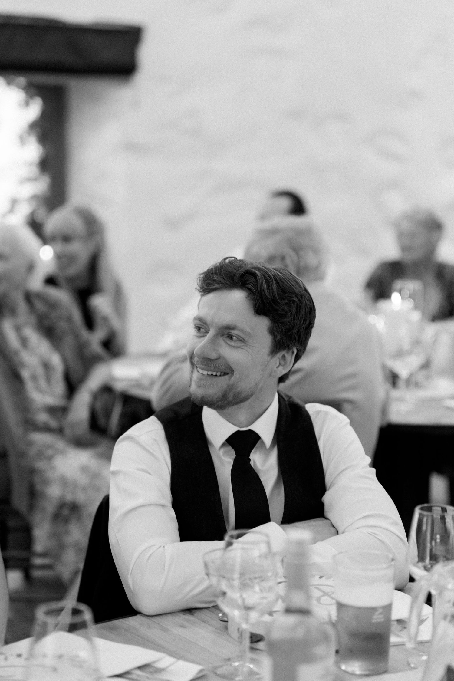 Wedding reception guests seated at dining tables with glassware in black and white.