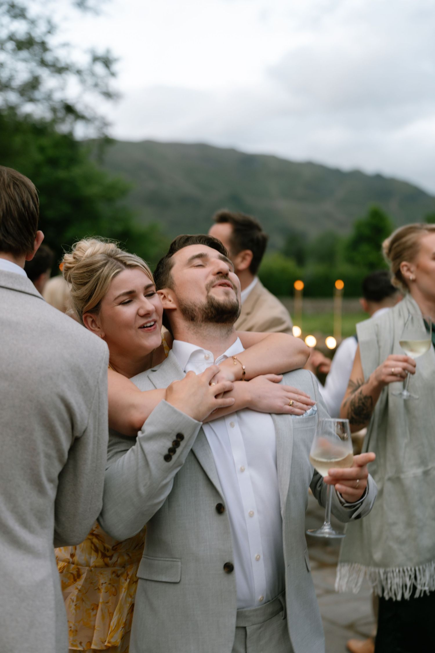 Wedding party celebrates with champagne toasts against mountain backdrop.