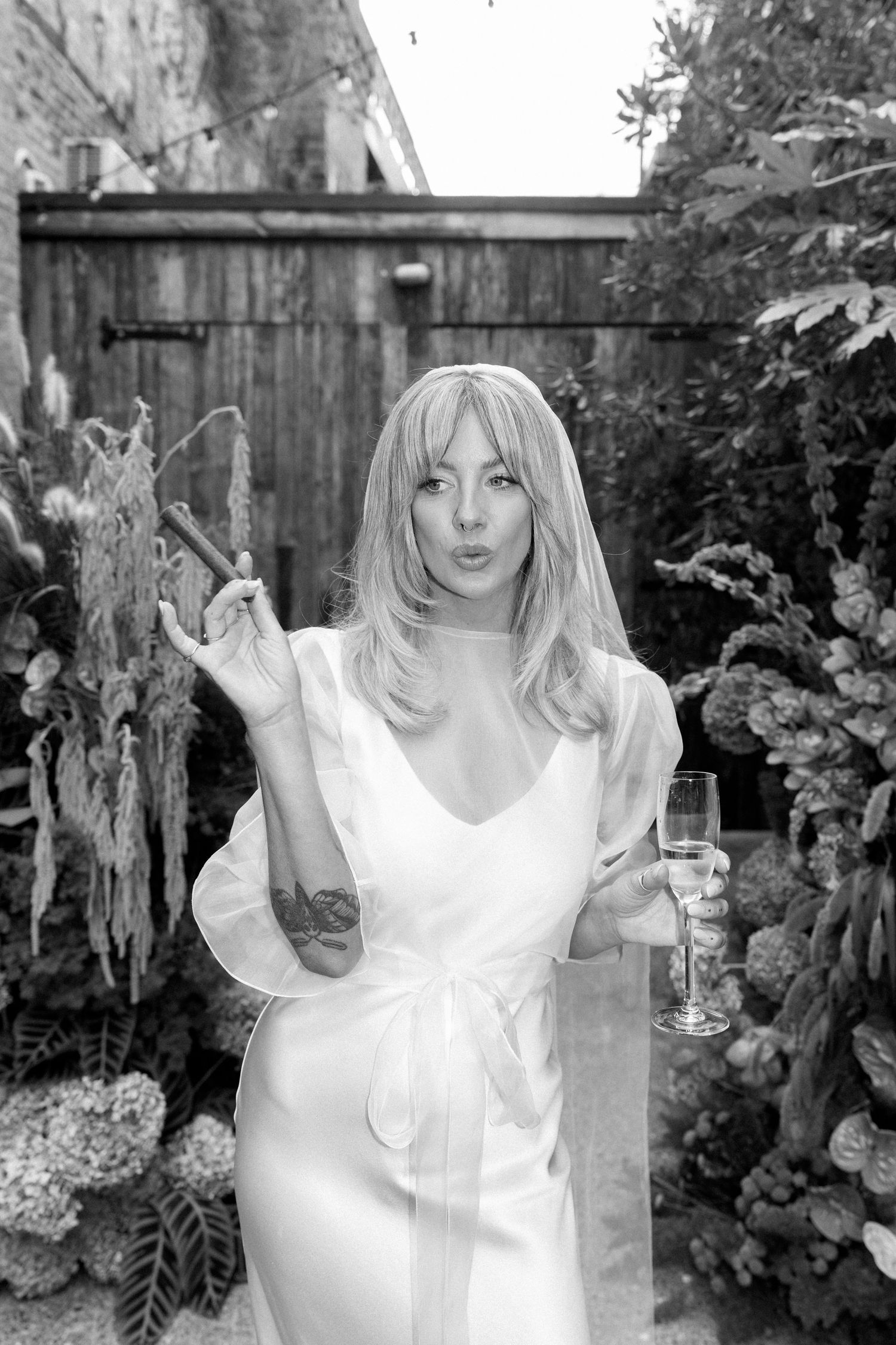 Playful black and white portrait series in garden setting with white dress and dramatic poses.