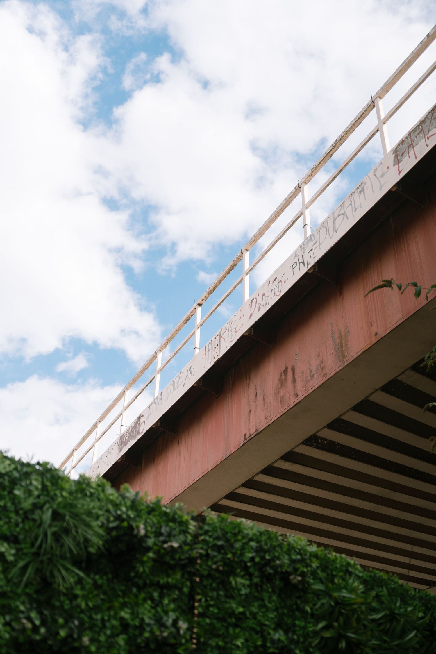 Concrete bridge structure against blue sky with white clouds and green foliage below.