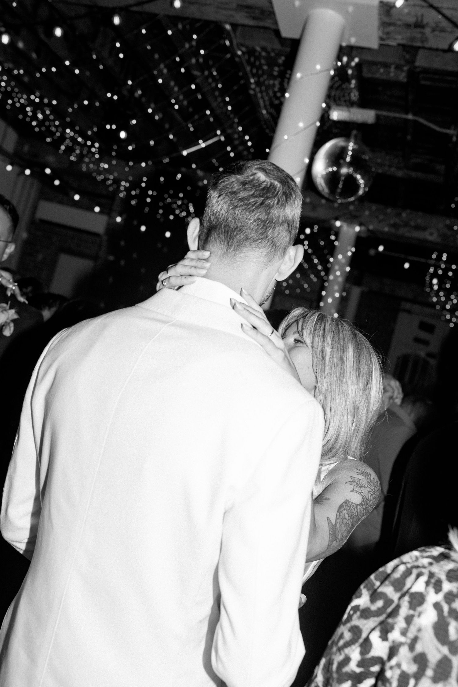 Black and white photo of couple dancing under twinkling lights at reception.